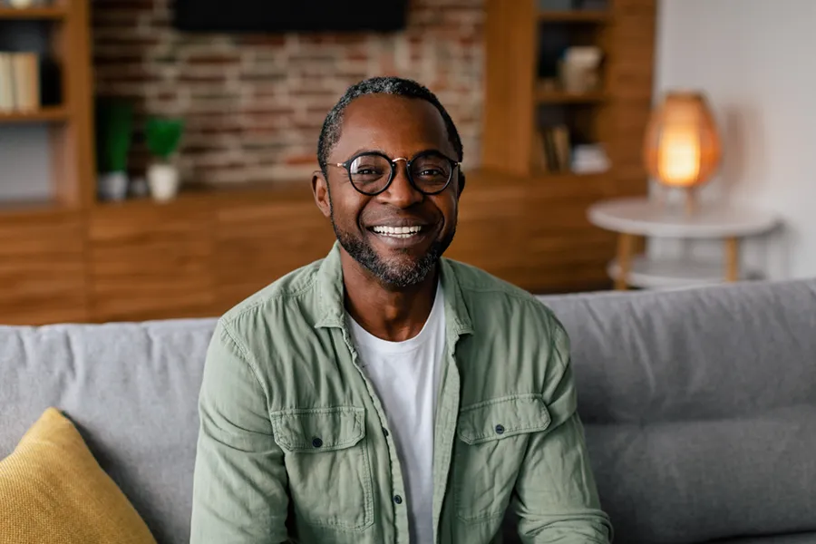 Andropause-Doctor A middle aged black man in a green button up shirt sits on his couch smiling, happy with his treatment for andropause and low testosterone from Better Life Carolinas of Charlotte in Charlotte Metro.