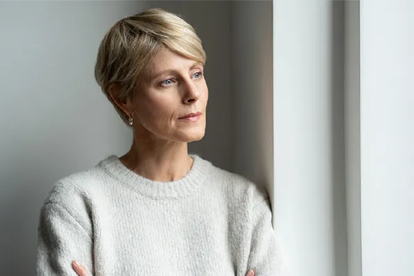 Chronic-Fatigue-Therapy A blond, middle-aged woman looks out the window with a tired expression. Get chronic fatigue treatment from Better Life Carolinas of Charlotte in Charlotte Metro.