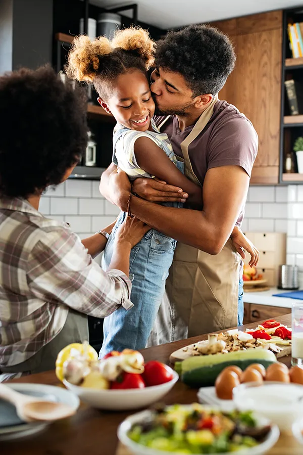 Gut-Health-Treatment A man holds his daughter and kisses her cheek as the family makes a healthy dinner in the kitchen. Get help for digestive issues and gut health from Better Life Carolinas of Charlotte in Charlotte Metro.