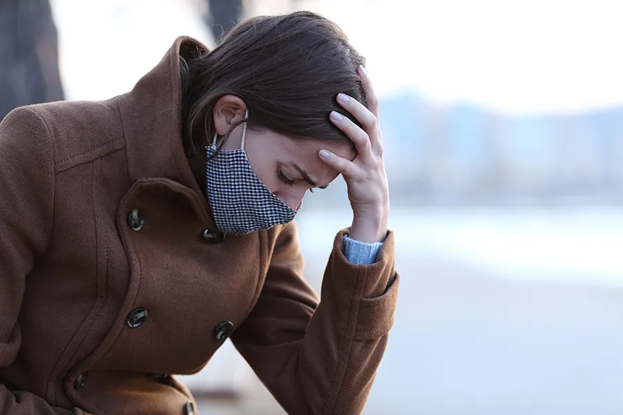 Post-Covid-Clinic A woman in a mask sits outside with her hand on her forehead in pain. Get long covid treatment from Better Life Carolinas of Charlotte in Charlotte Metro.