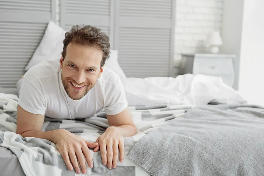 Sexual-Wellness-for-Men-Doctor A man in a t-shirt lies on his stomach in bed smiling, happy with his sexual wellness treatments from Better Life Carolinas of Charlotte in Charlotte Metro.