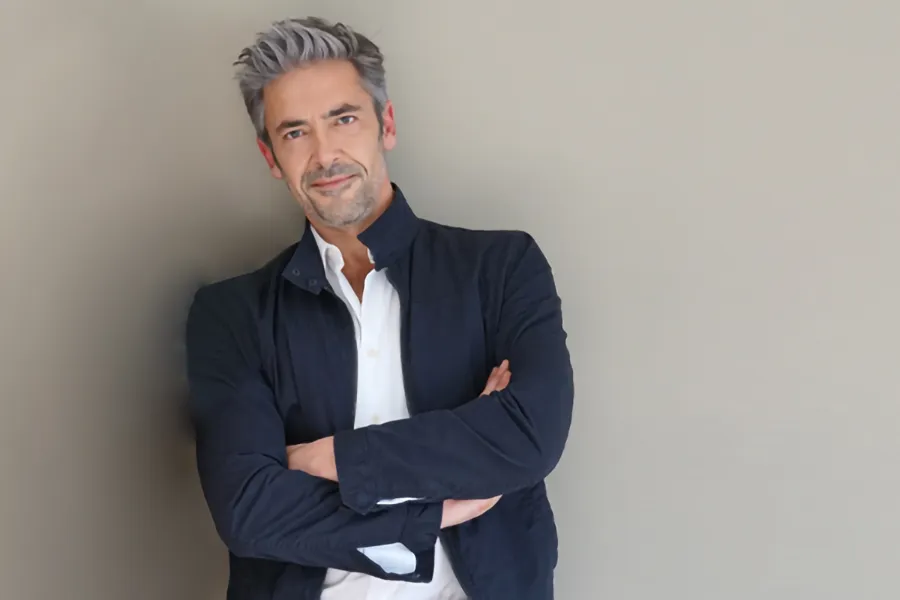 Testosterone-Low-T-Solutionsn-Clinic A middle-aged man in a white shirt and dark blue jacket leans against a gray wall smiling. Get testosterone for Low T from Better Life Carolinas of Charlotte in Charlotte Metro.